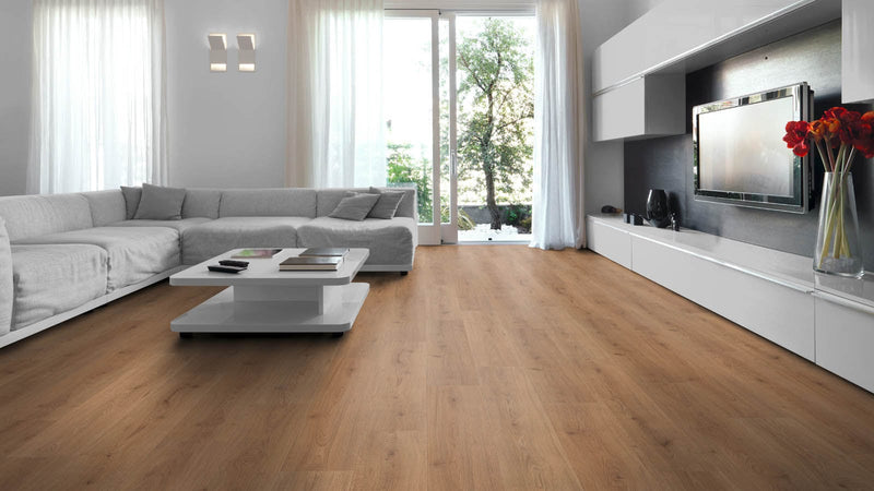 A modern living room with light brown floating laminate wood flooring, featuring a white sectional sofa, a low white coffee table, and a built-in wall-mounted television on a white media console.